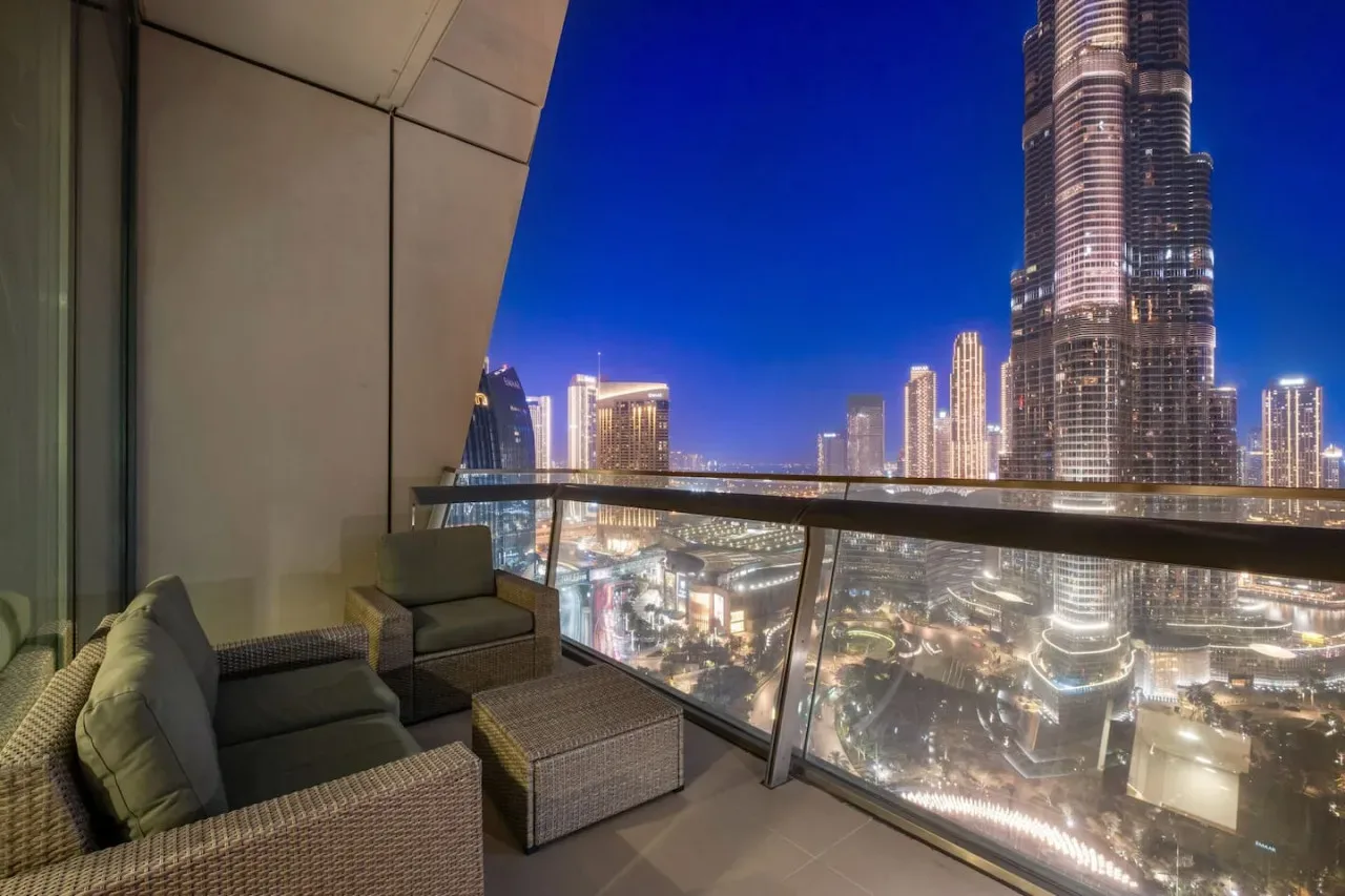 A balcony seating area overlooks a brightly lit city skyline at night.