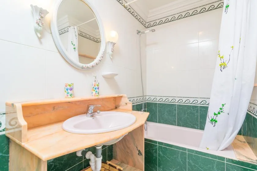 A tiled bathroom with a sink, oval mirror, and bathtub behind a shower curtain.
