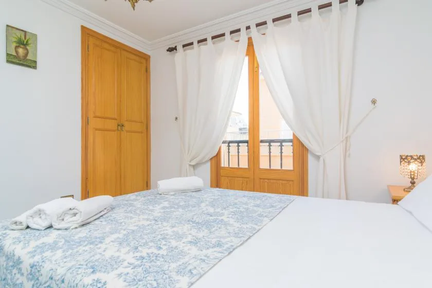 A bedroom with a bed and white curtains framing a glass door.