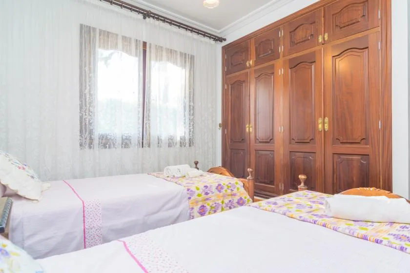 A bedroom with beds beside a large wooden wardrobe and a curtained window.
