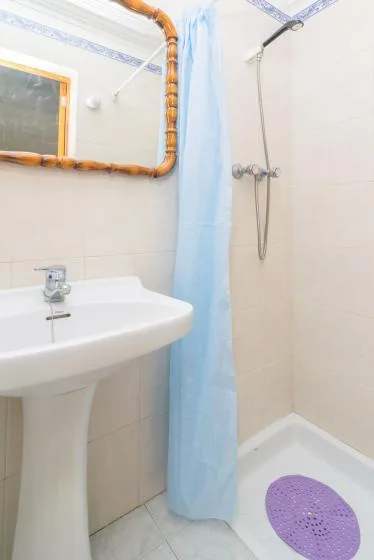 A bathroom with a pedestal sink and a shower behind a blue curtain.