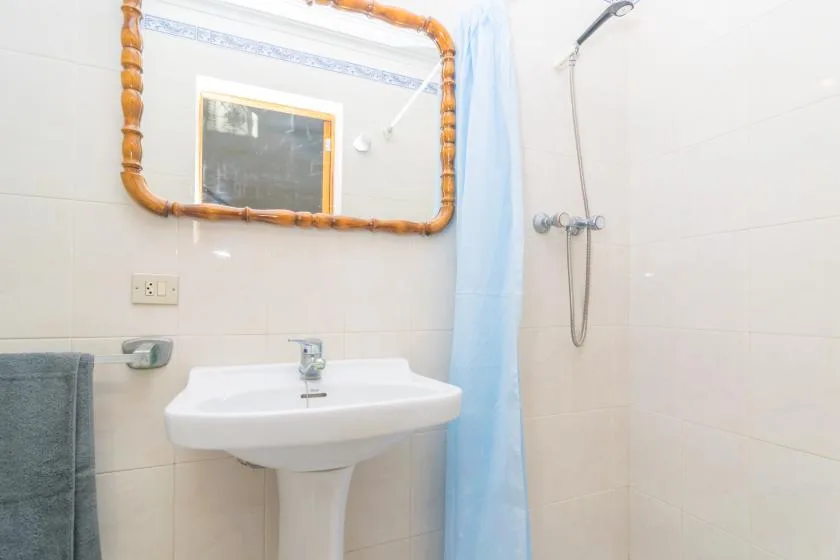 A tiled bathroom with a pedestal sink and a shower beside a blue curtain.