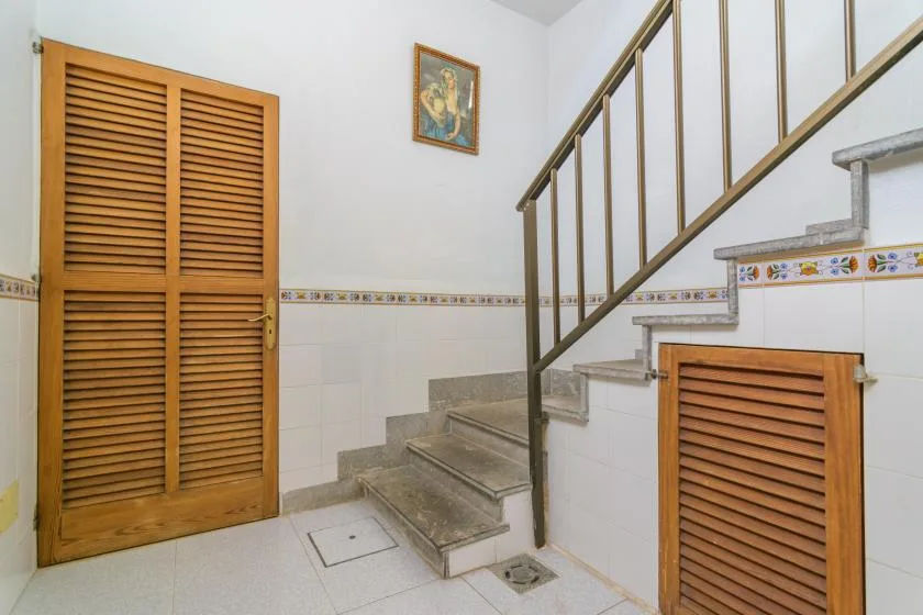 A tiled interior stairwell with a metal railing and wooden louvered doors.