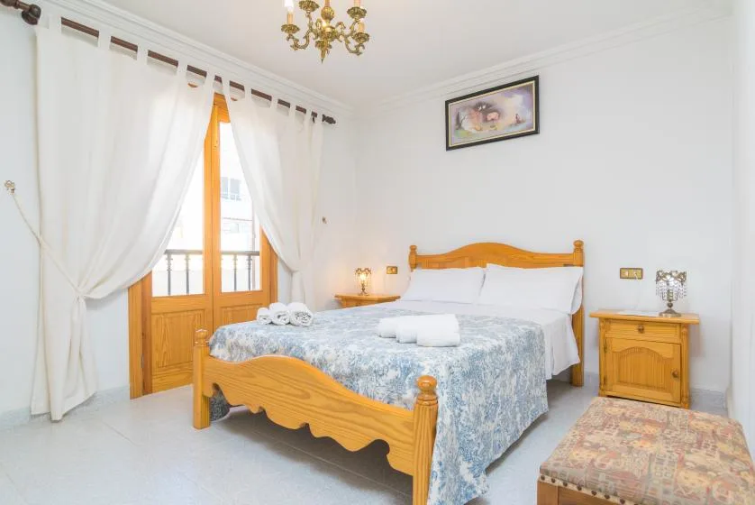 A bedroom with a wooden bed, patterned bedding, and curtains beside the window.