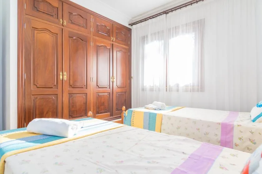 A bright bedroom with two beds and a large wooden wardrobe.