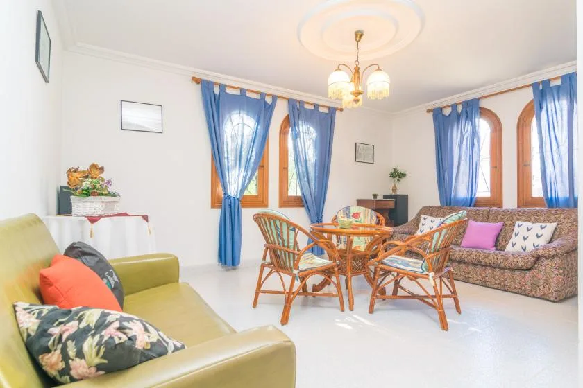 A bright living room with seating and a round dining table beside blue-curtained windows.