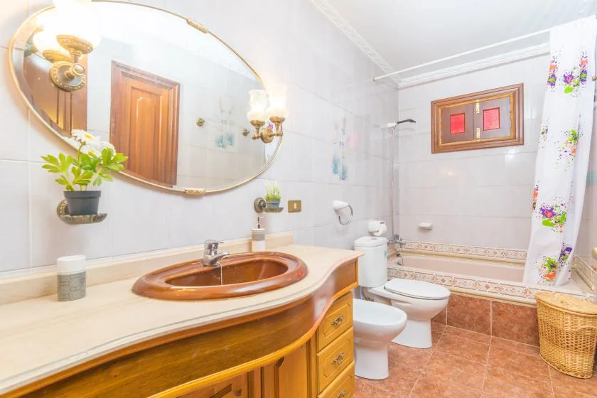 A bathroom with a wooden vanity, oval mirror, and bathtub behind a floral curtain.