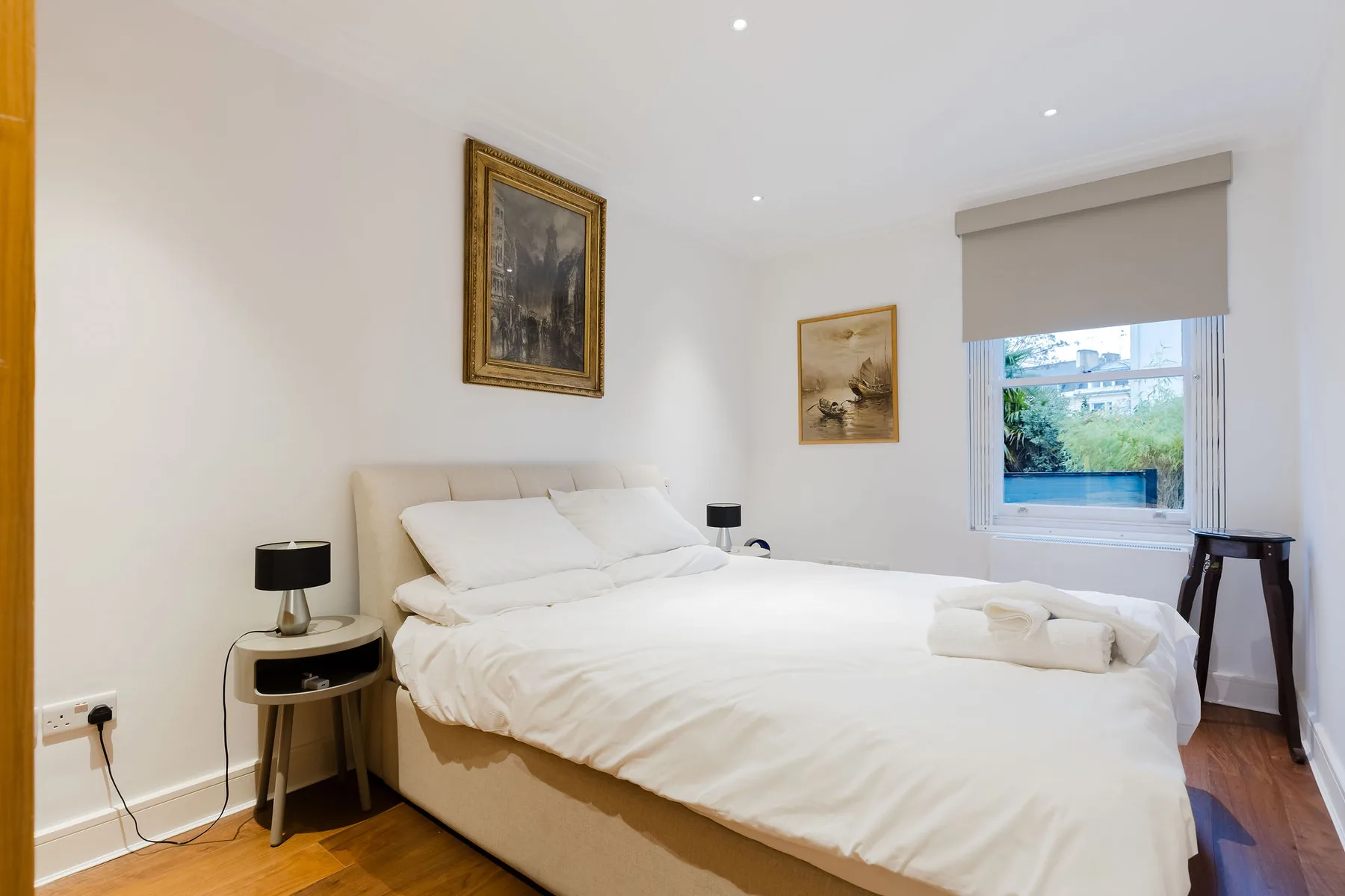Un dormitorio luminoso con una cama grande, cuadros enmarcados y una ventana.