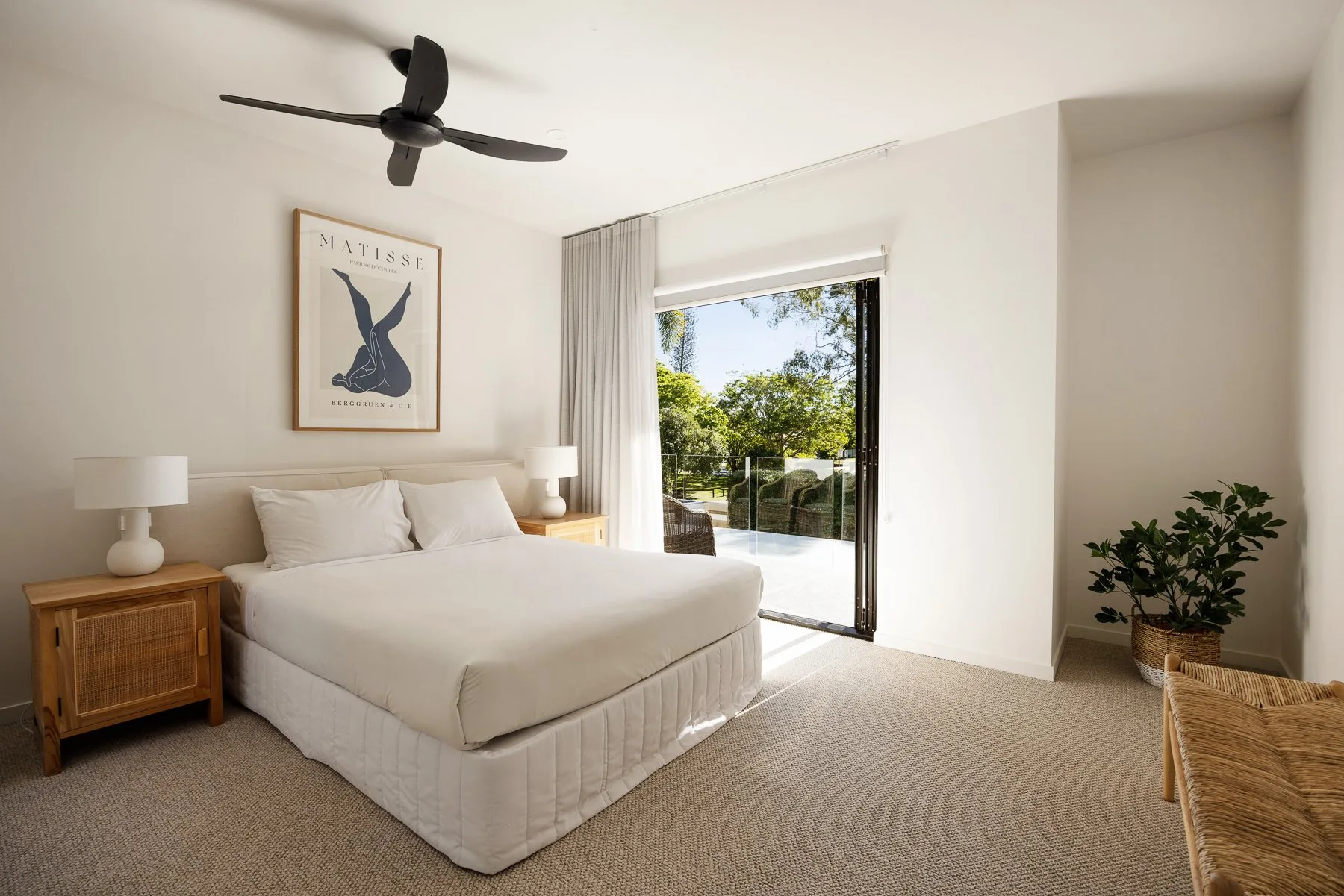 A bright bedroom with a bed, bedside tables, and a glass door opening onto greenery.