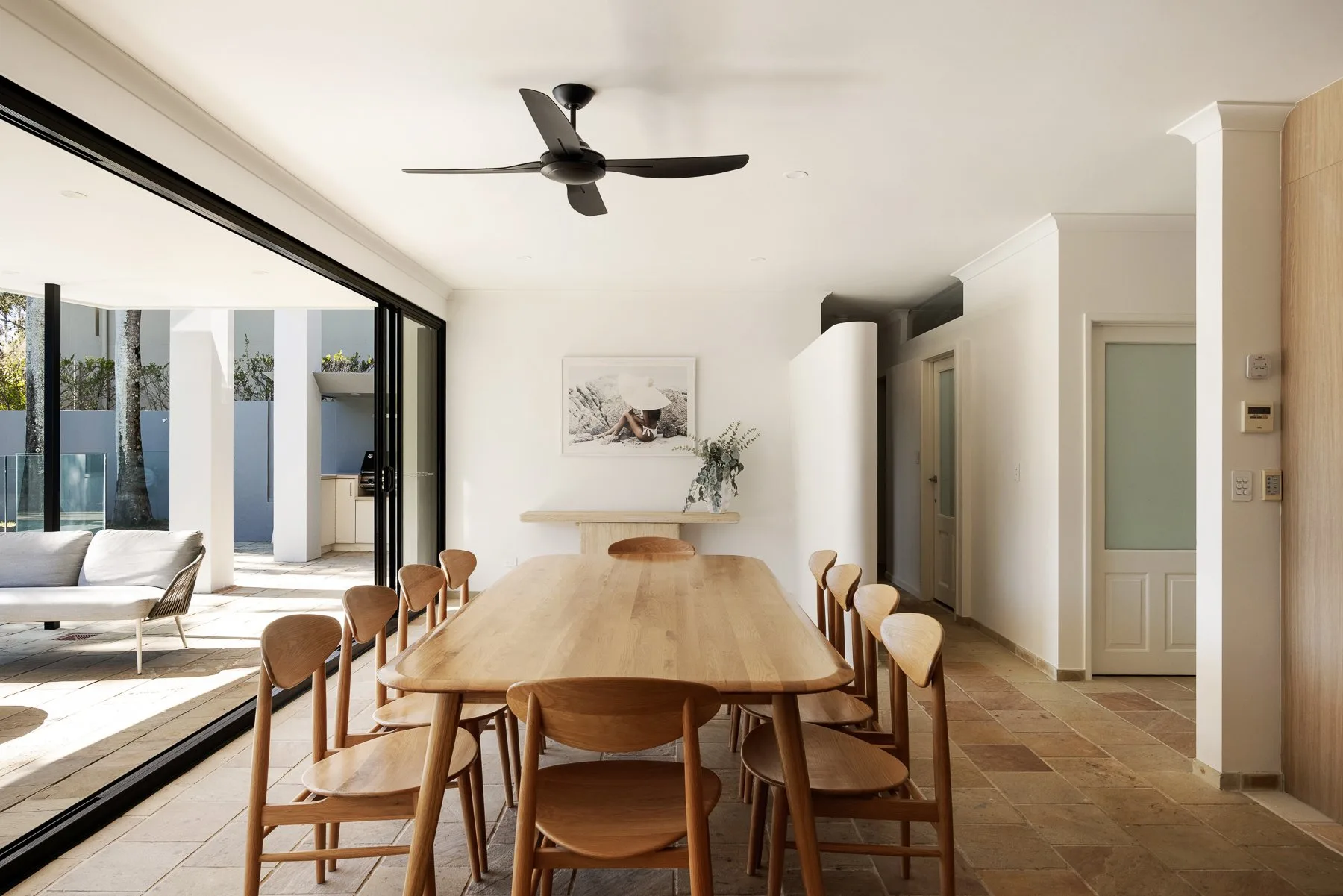 A bright dining area with a long wooden table beside large glass doors.