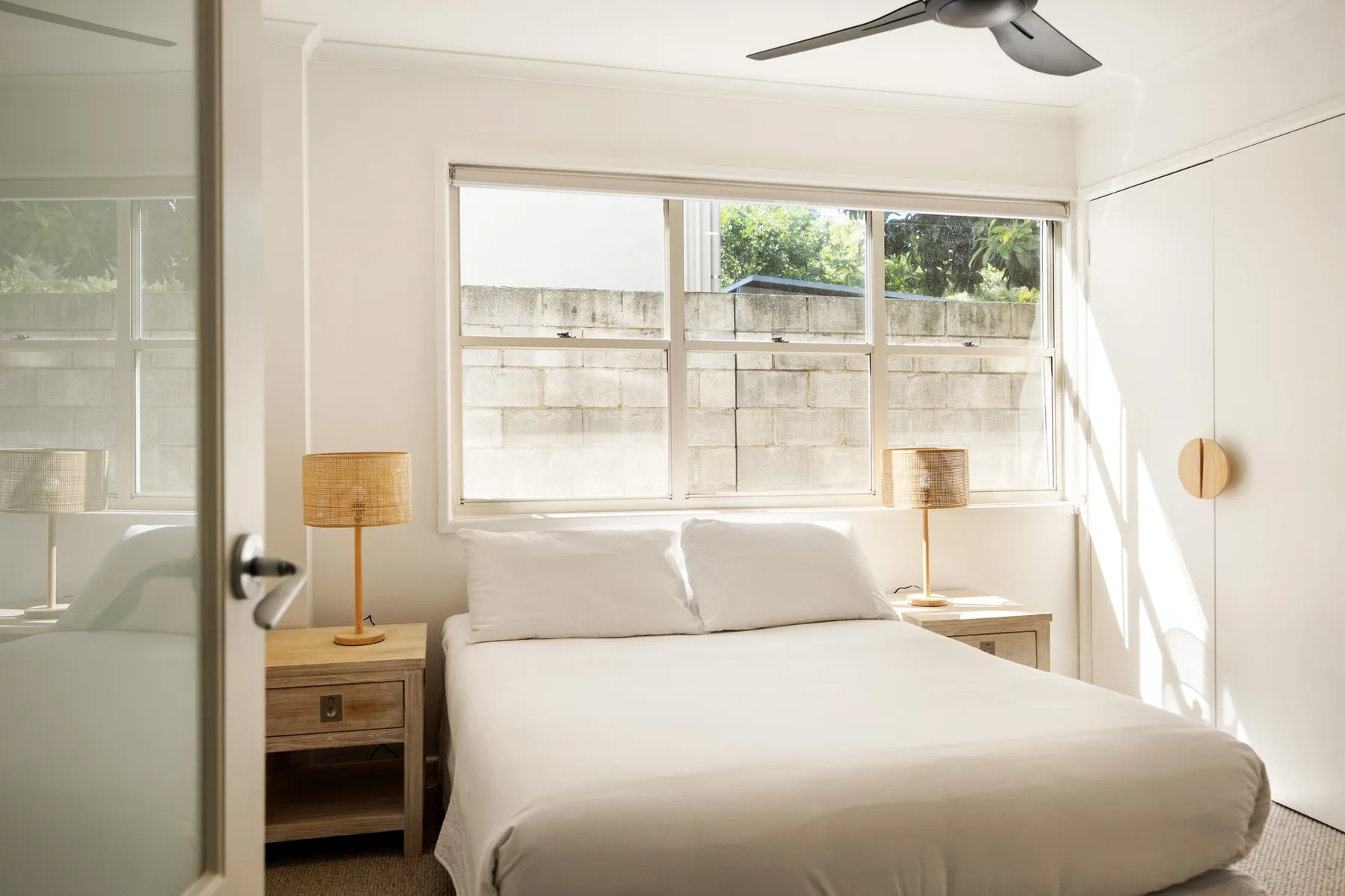 A bright bedroom with a neatly made bed beneath a wide window.