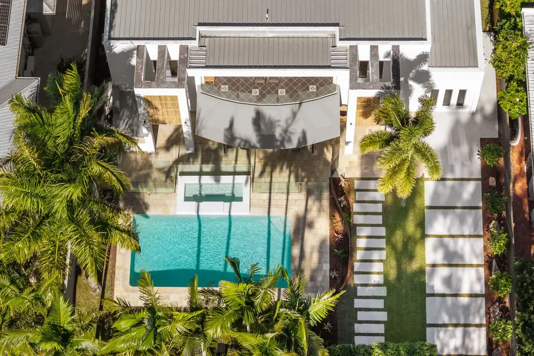 An aerial view shows a swimming pool beside a modern house and garden.