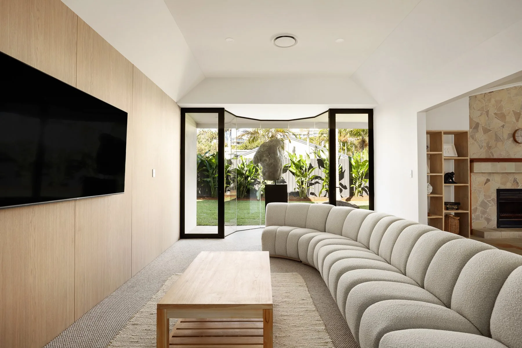 A bright living room with curved seating facing a large television and garden views.