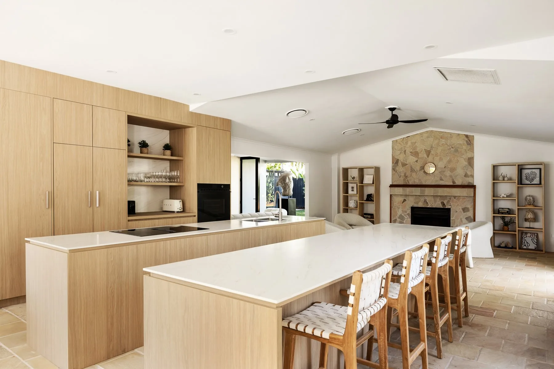 A bright open-plan kitchen and dining area with a long island and stone fireplace.
