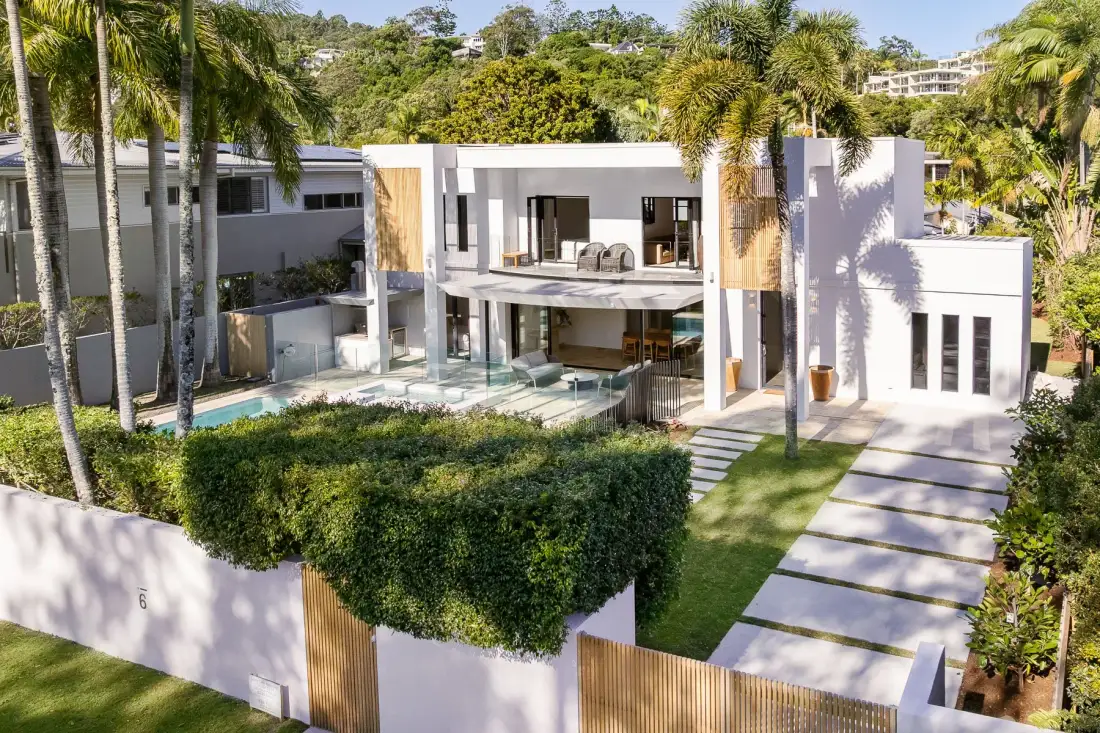 A modern white house surrounded by tropical landscaping, with a paved walkway leading to the entrance.