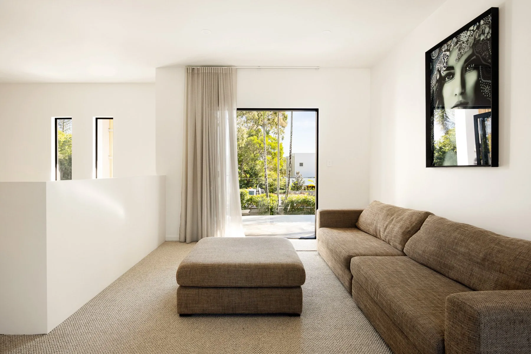 A bright living room with seating and a sliding glass door opening to greenery.