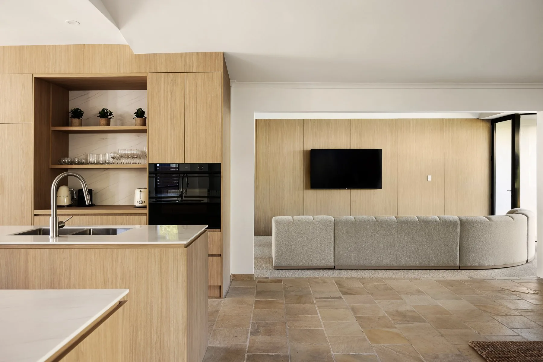A modern open-plan kitchen and living area with a television mounted on the wall.