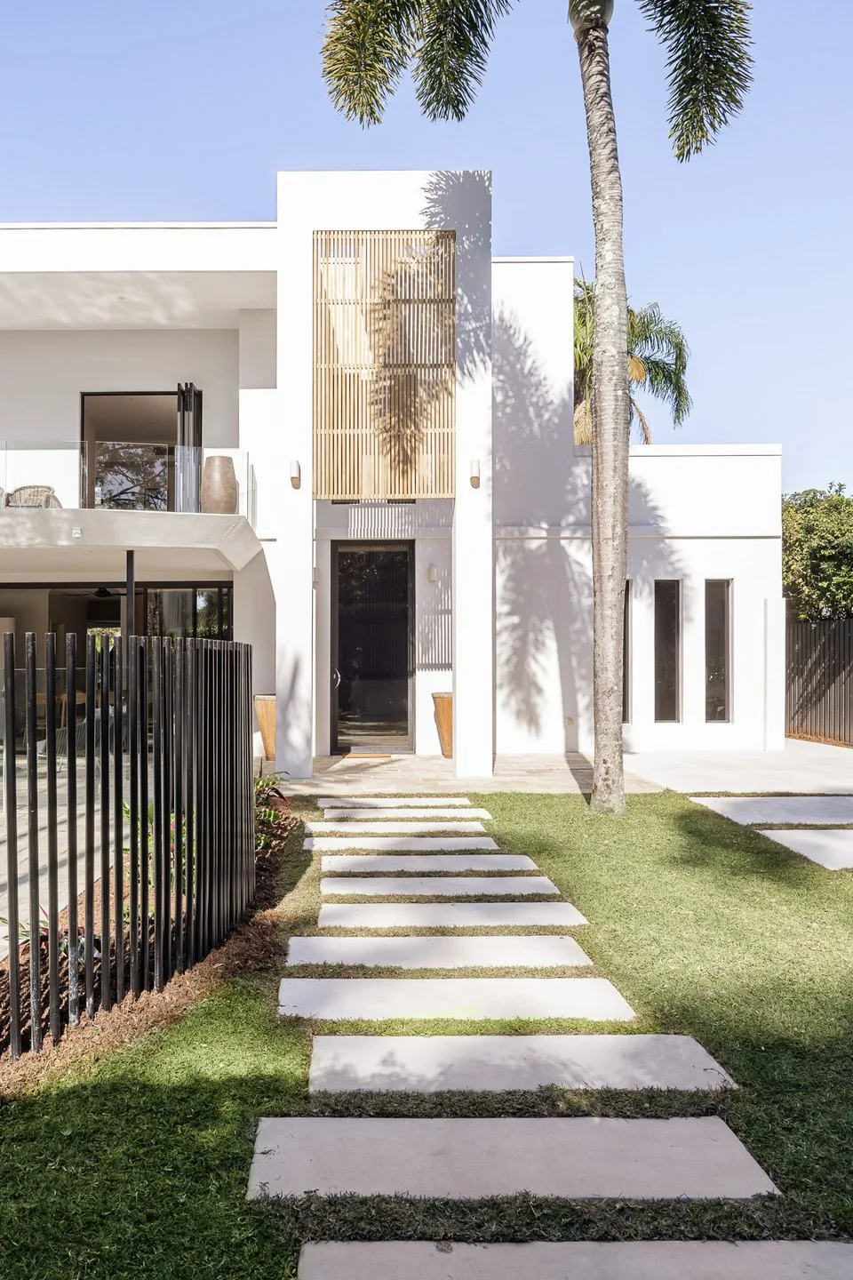 A modern white house stands behind a stepping-stone path across a green lawn.