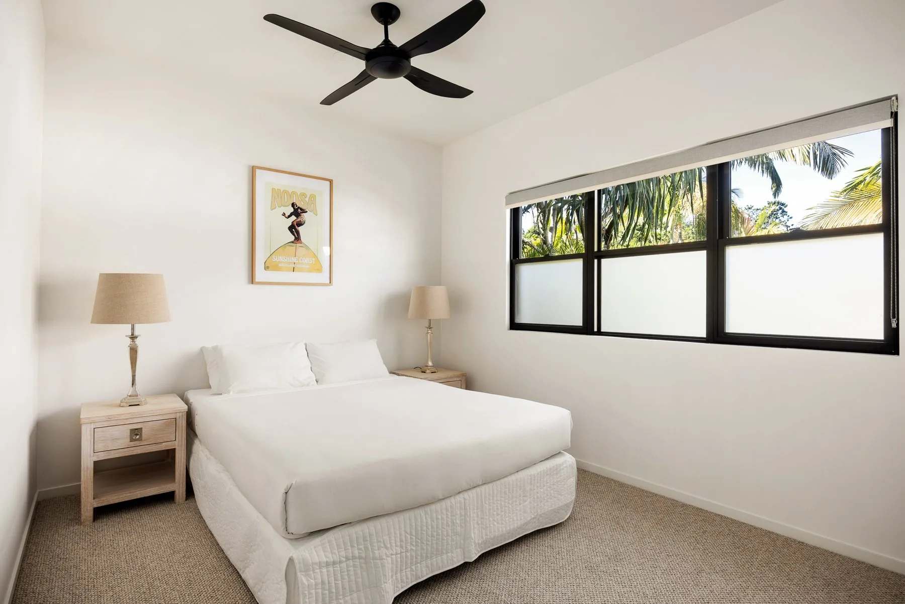 A bedroom with a white bed and a wide window overlooking palm trees.