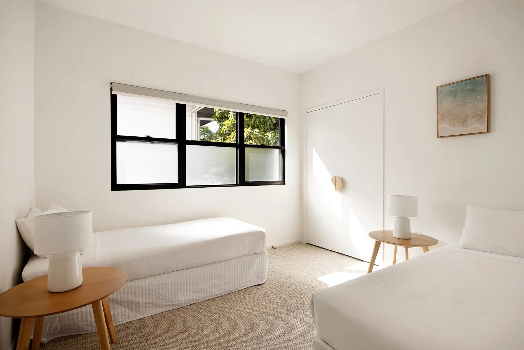 A bright bedroom with a large window and simple furnishings.