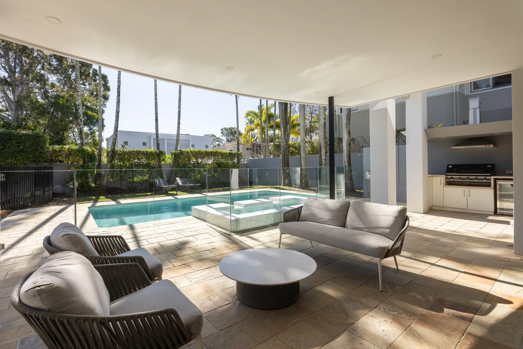 A covered patio with seating overlooks a swimming pool and landscaped garden.