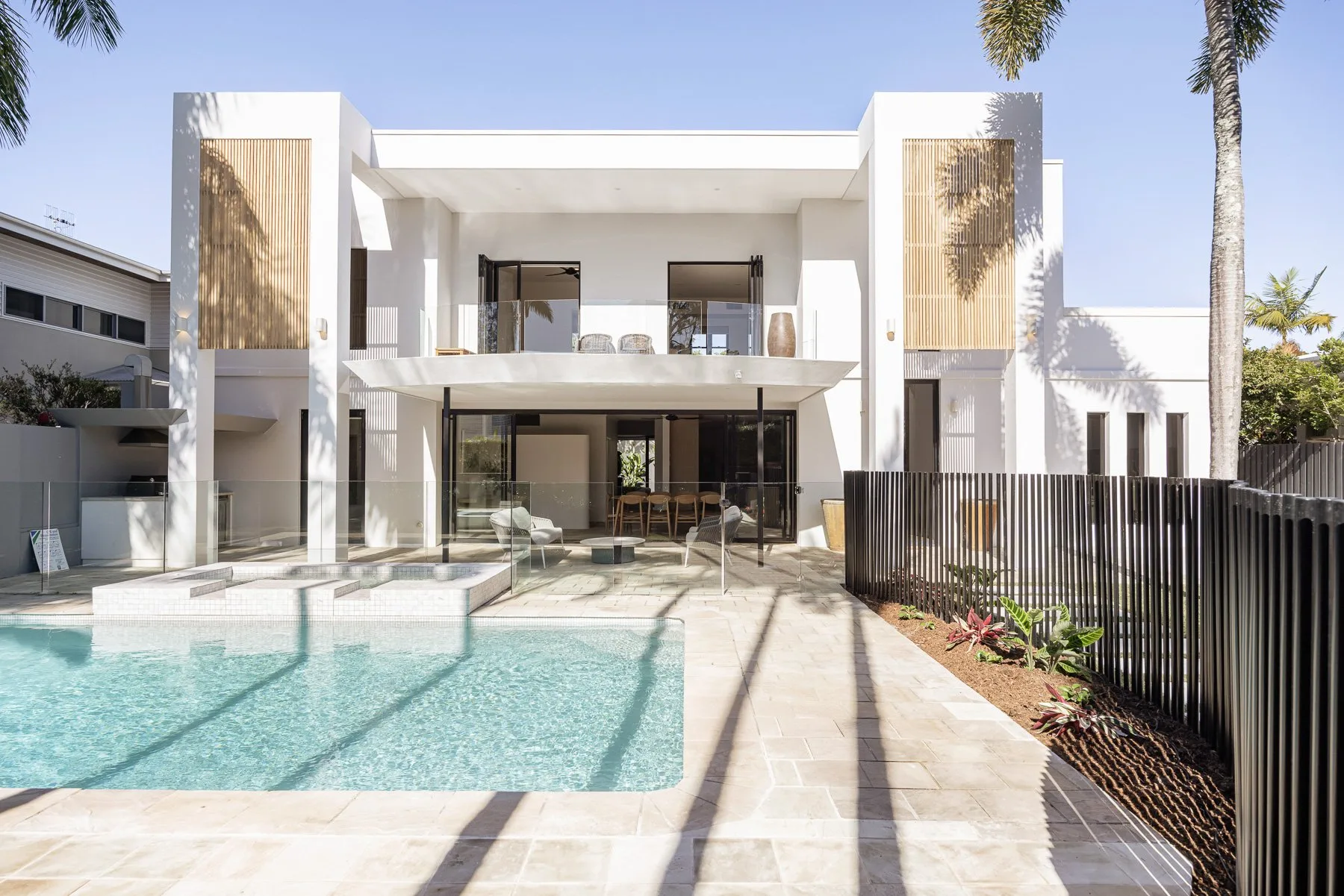A modern two-story house overlooks a swimming pool and paved patio.