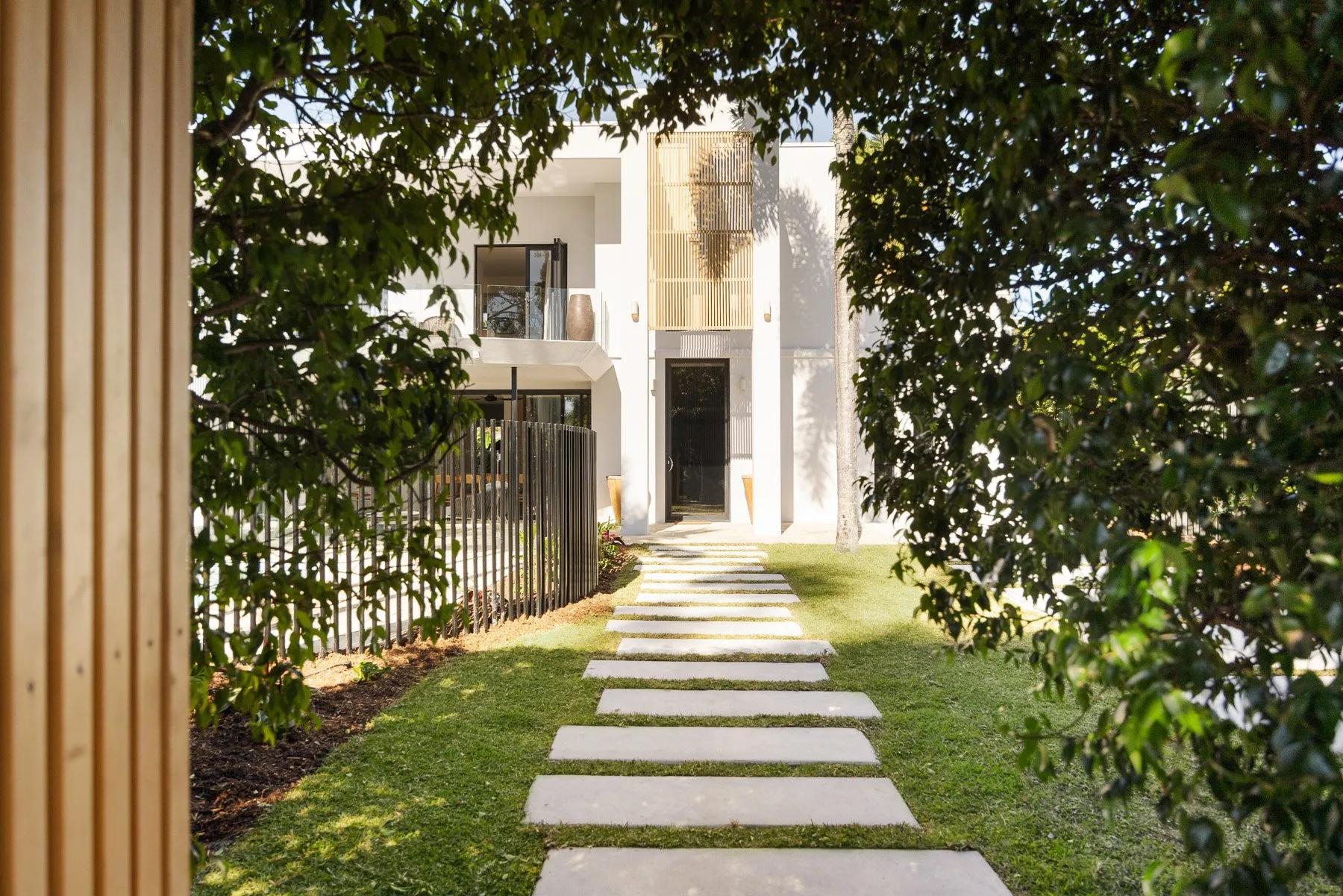A paved garden path leads through greenery toward a modern white house.