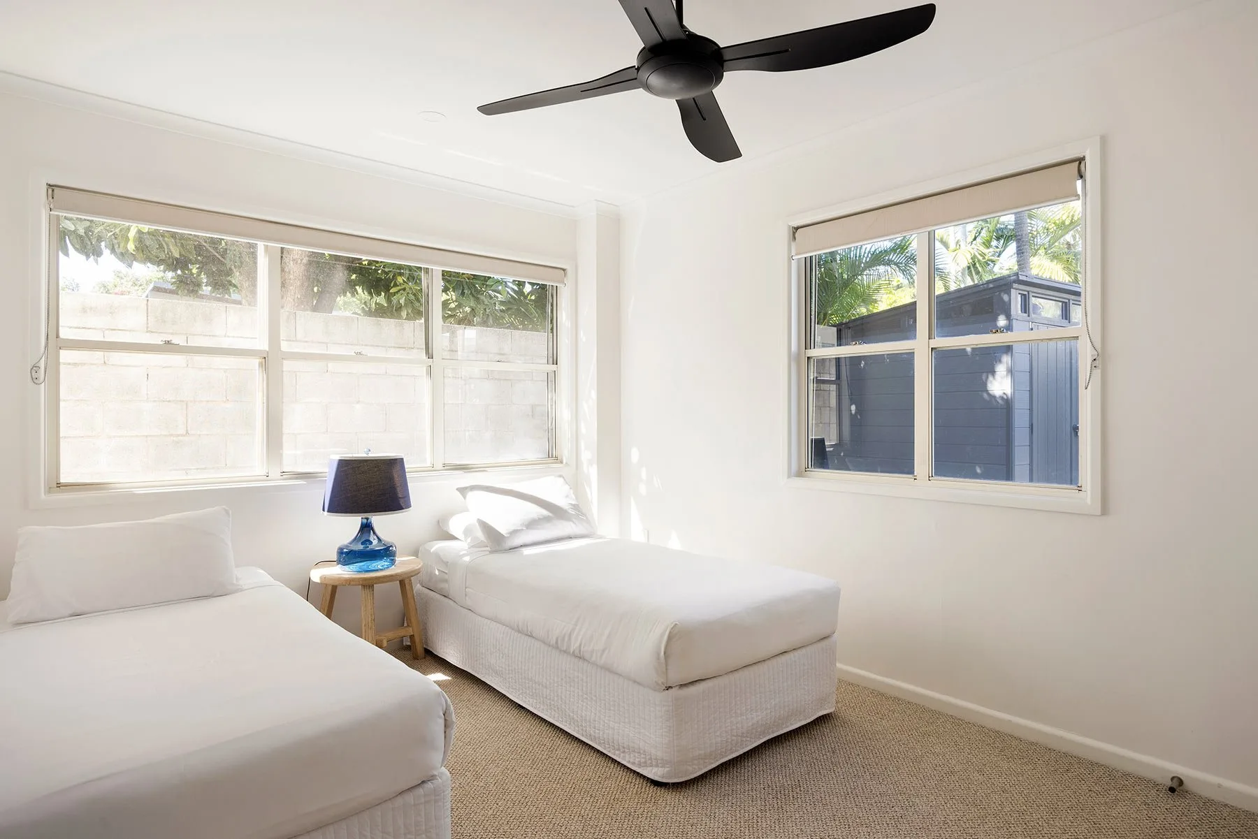 A bright bedroom with two beds and windows overlooking greenery.