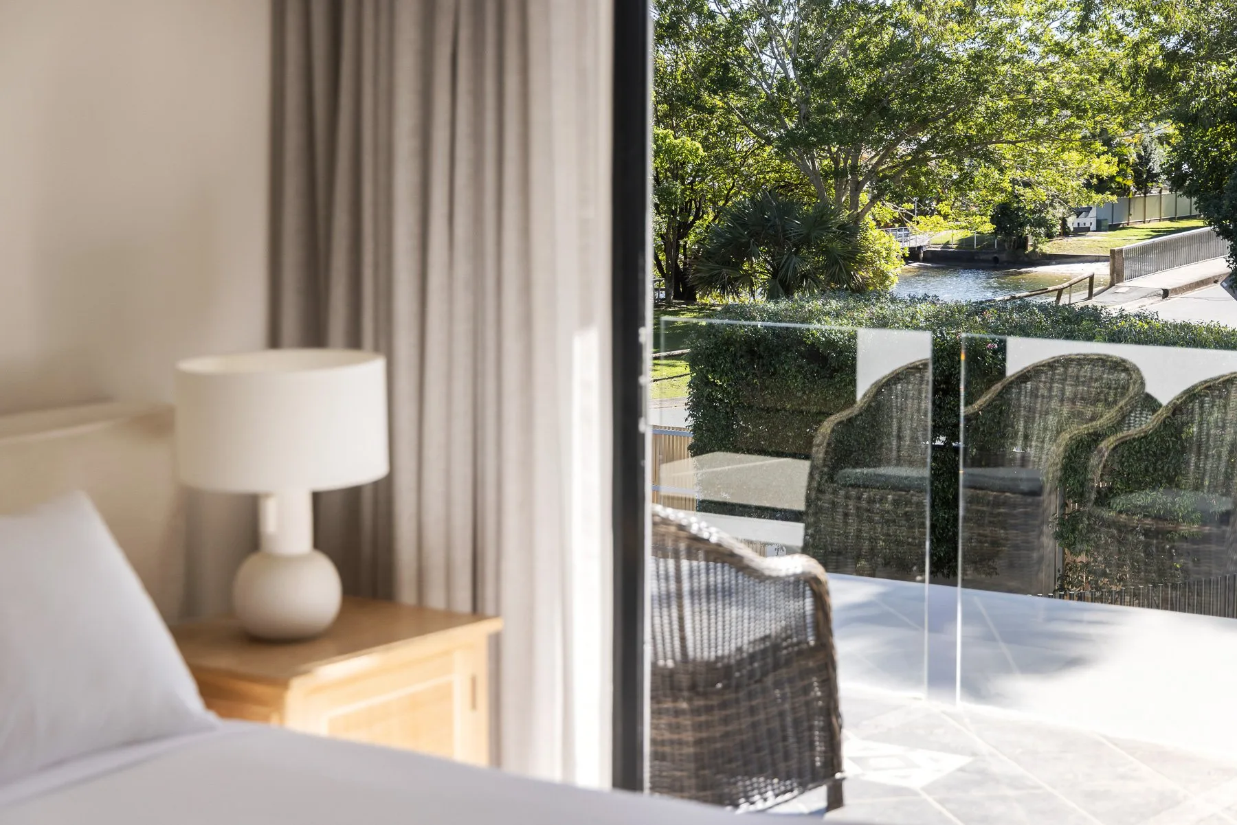 A bedroom opens onto a patio with outdoor seating and leafy trees beyond.