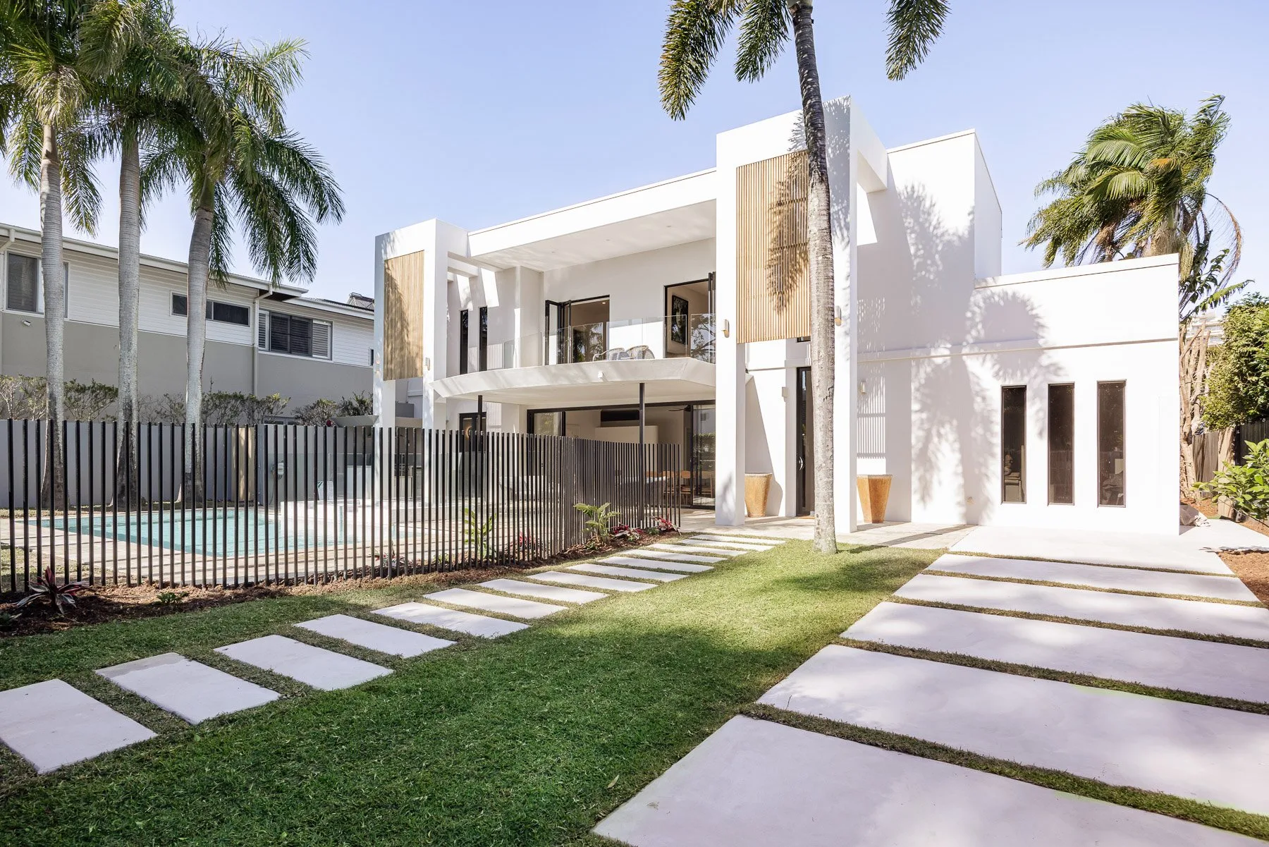 A modern white house with a lawn, palm trees, and a stepping-stone path.