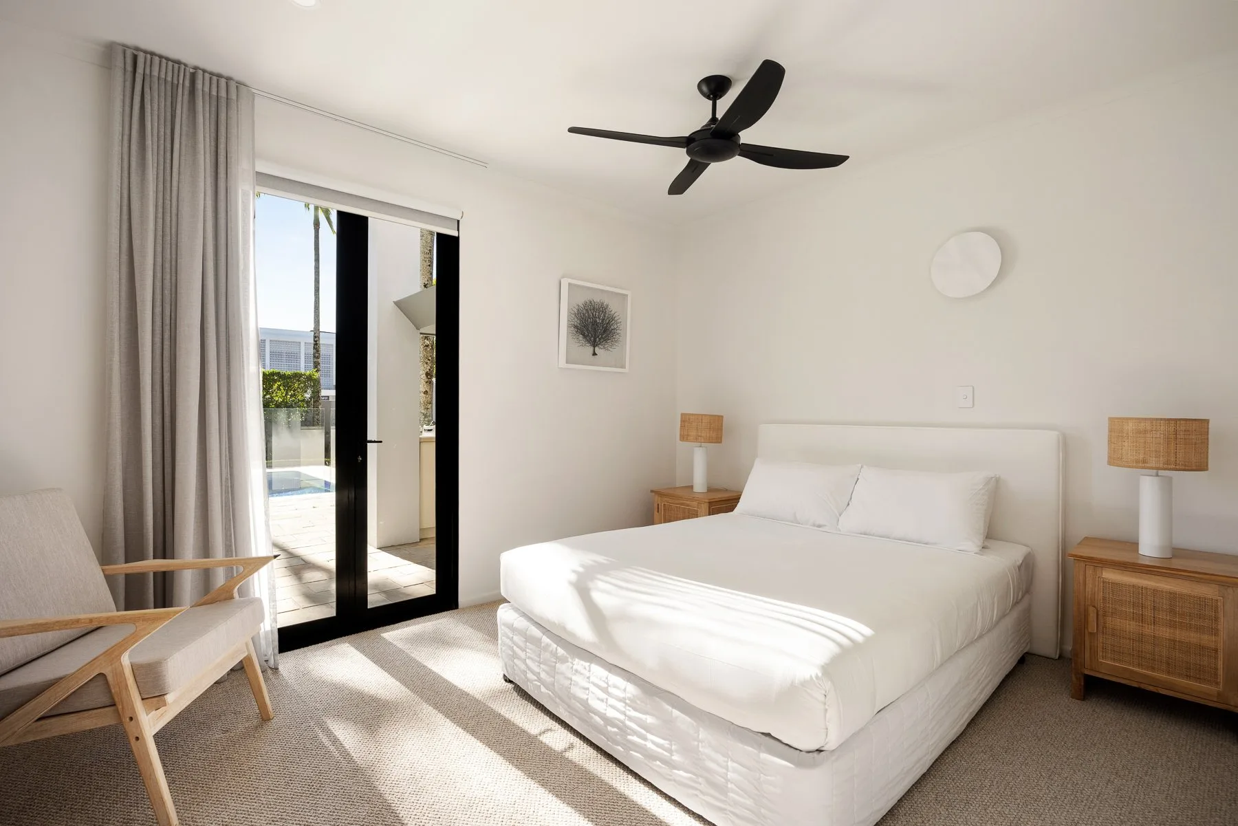 A bright bedroom with a white bed and sliding glass doors opening onto a patio.