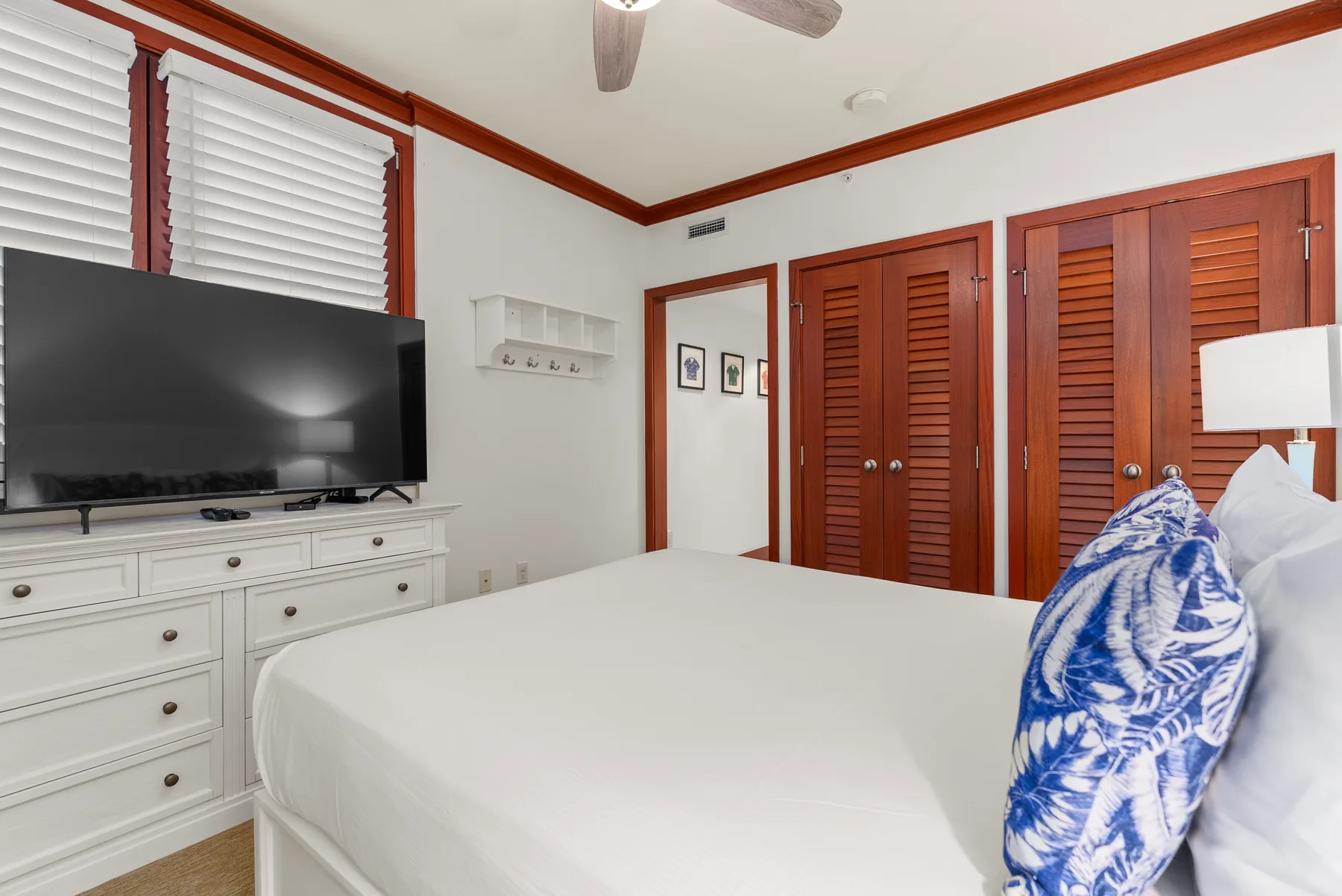 Un dormitorio con una cama blanca, un televisor y puertas de lamas de madera.