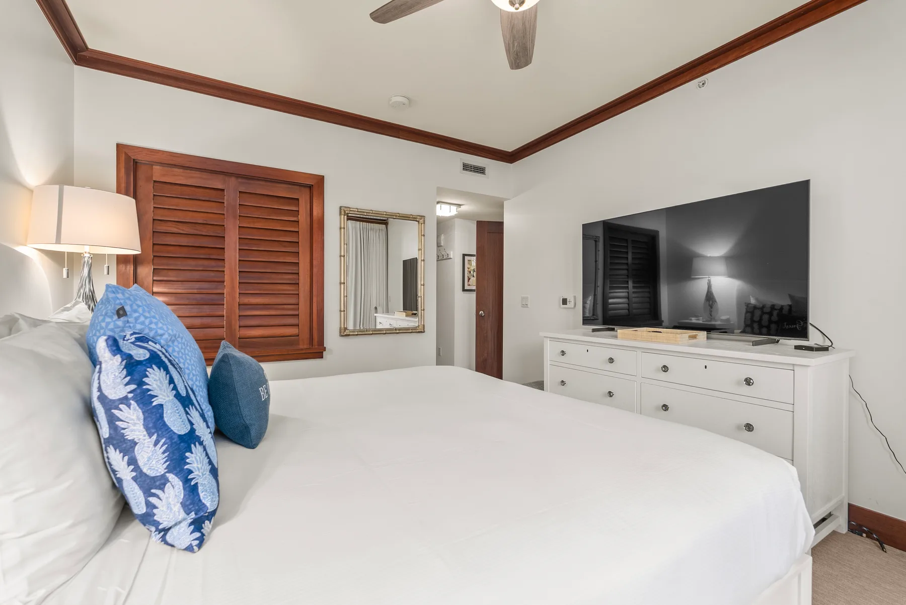 Un dormitorio con una cama blanca, persianas de madera y un televisor sobre una cómoda.