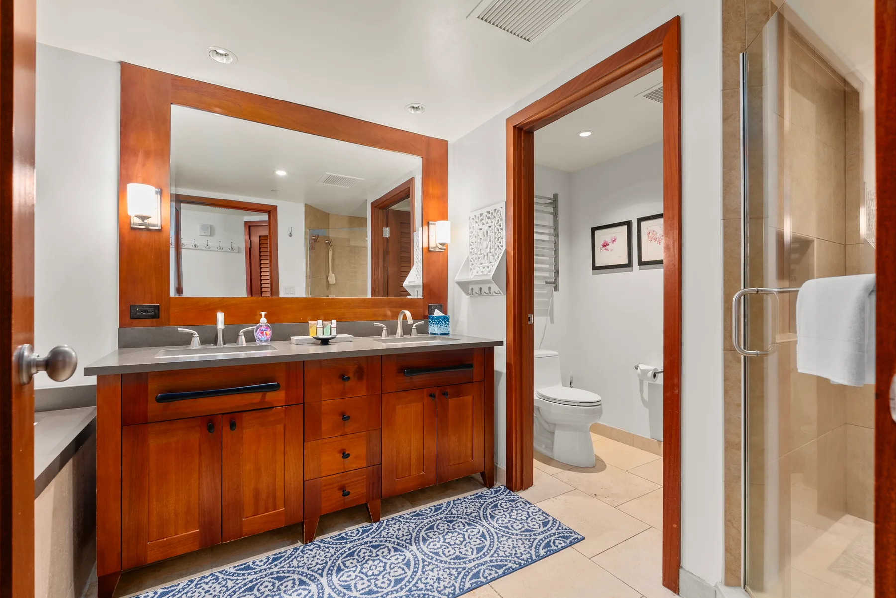 Un lavabo de baño con un espejo amplio, junto a una puerta abierta hacia la zona del inodoro.