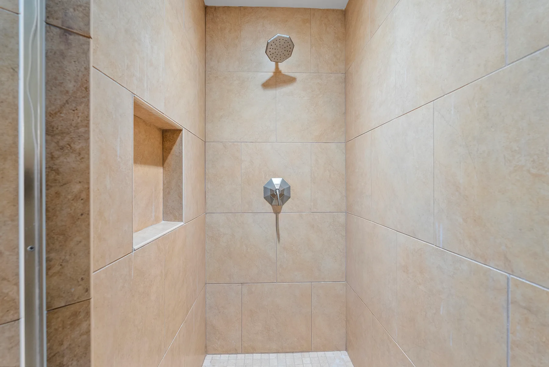 Una ducha con azulejos, un cabezal de pared y un nicho empotrado.