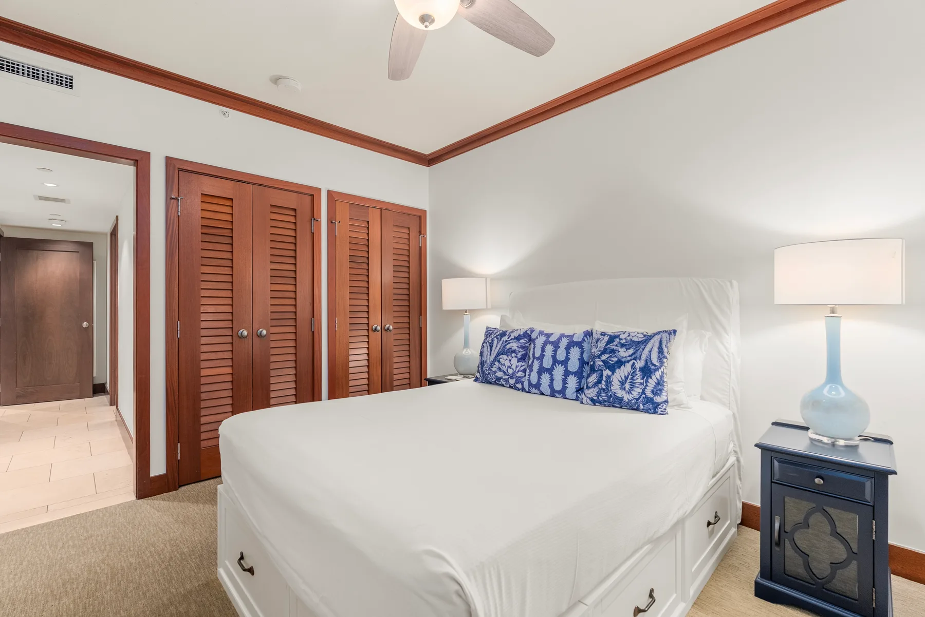 Un dormitorio con una cama blanca, almohadas estampadas azules y puertas de armario de madera.