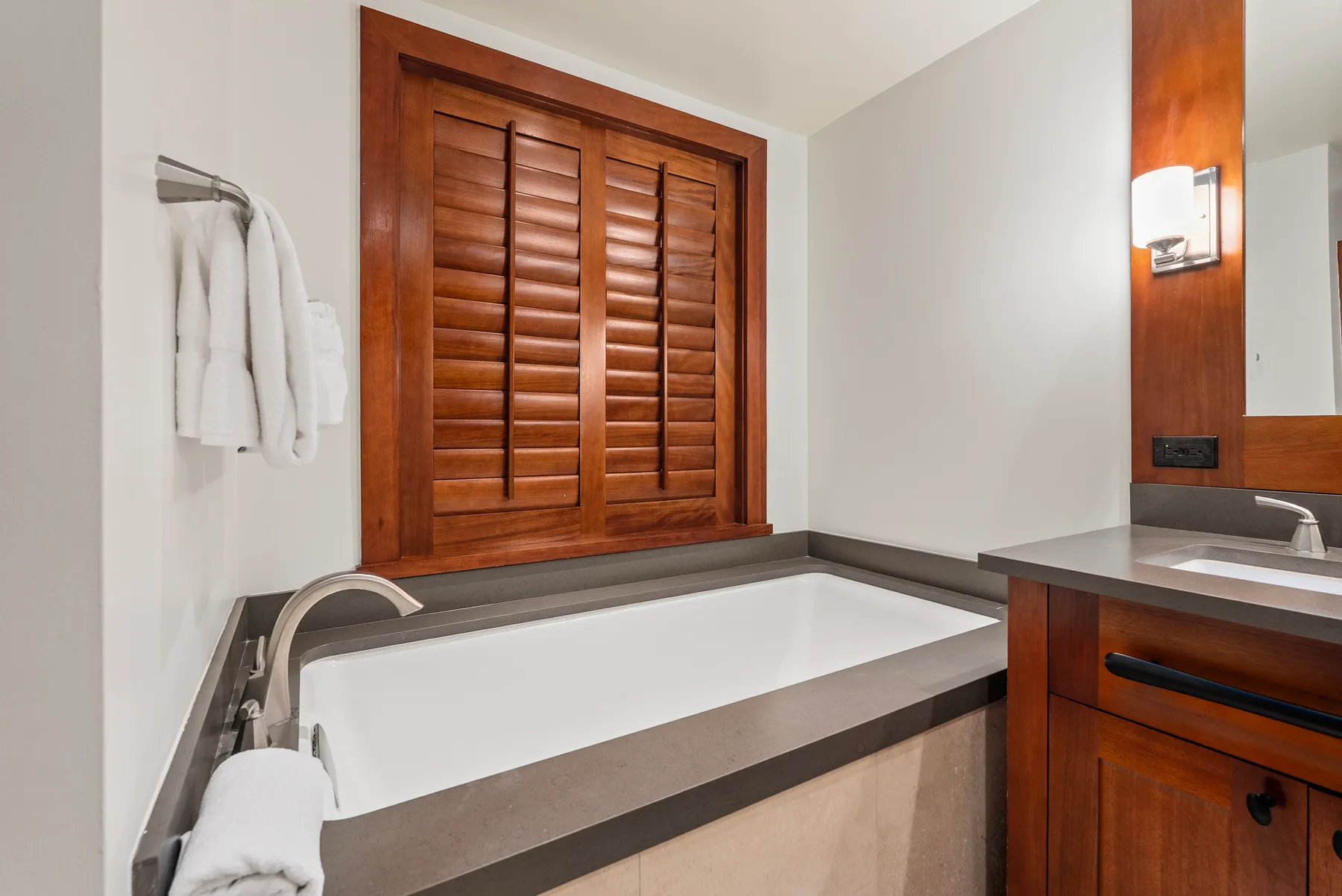 Un baño con una bañera empotrada bajo persianas de madera.