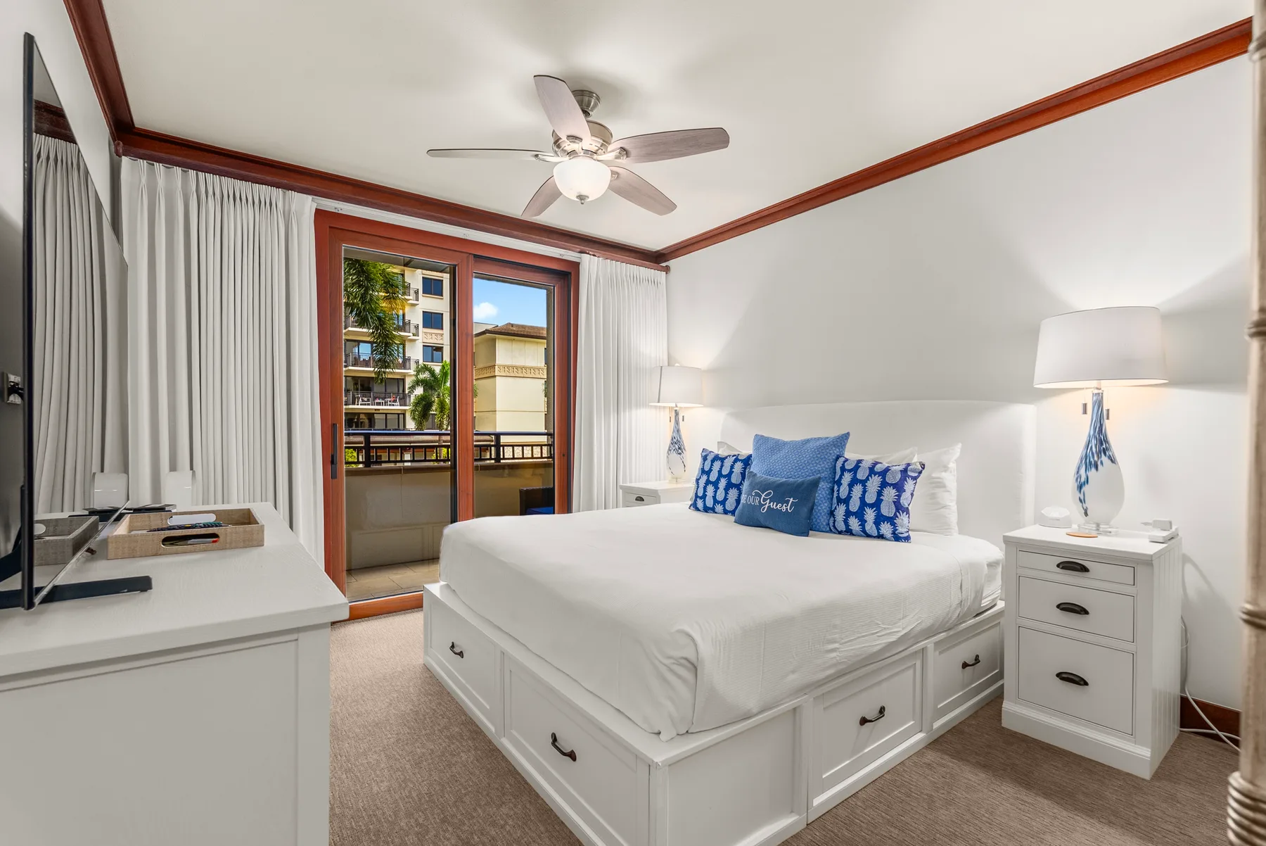 Un dormitorio luminoso con una cama blanca y puertas de vidrio que dan a un balcón.