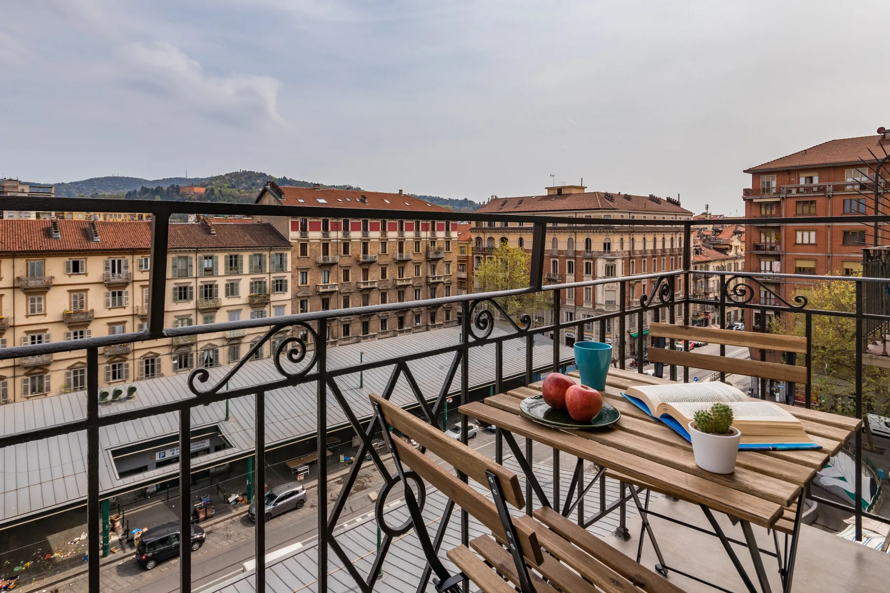 A rooftop terrace overlooks city buildings, with a wooden table and chairs nearby.