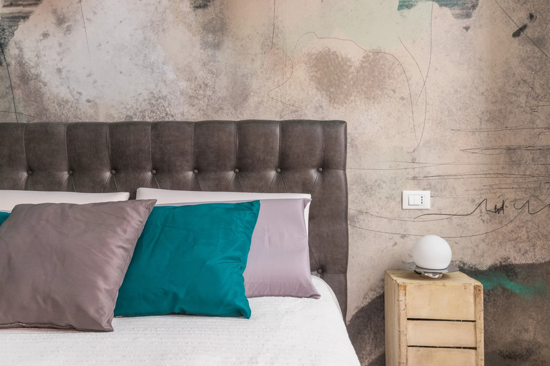 A bedroom with a tufted headboard, colorful pillows, and a wooden bedside table.