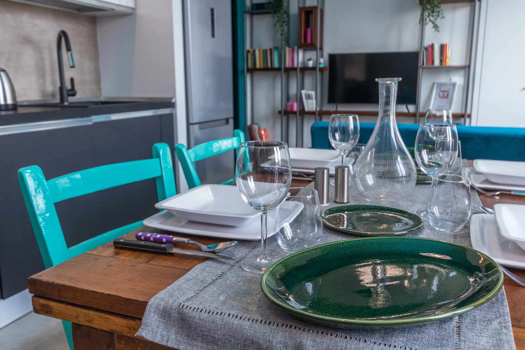 A dining table is set with plates and glassware in a modern kitchen and living area.