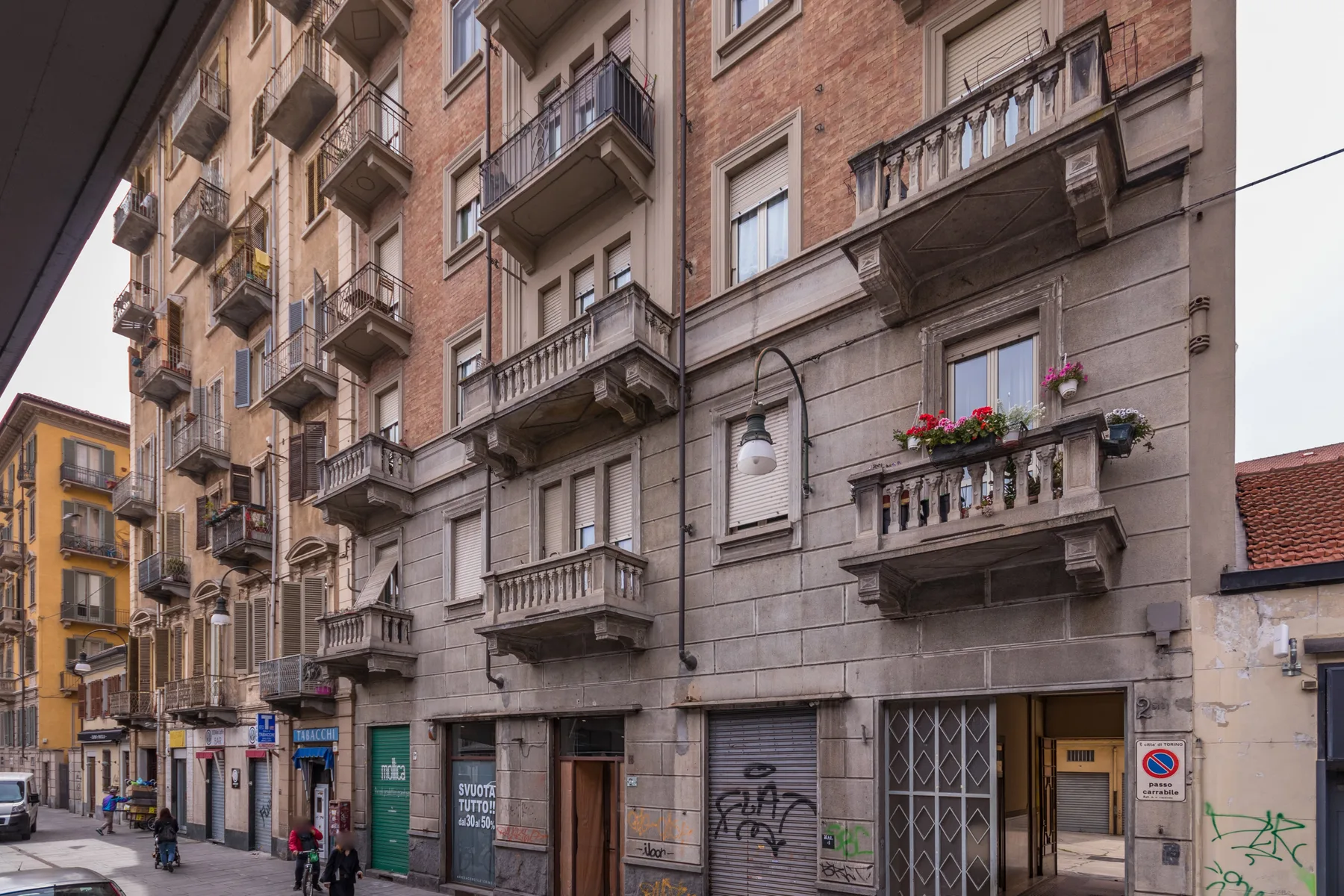 Street scene with a tall apartment building, balconies, and storefronts.