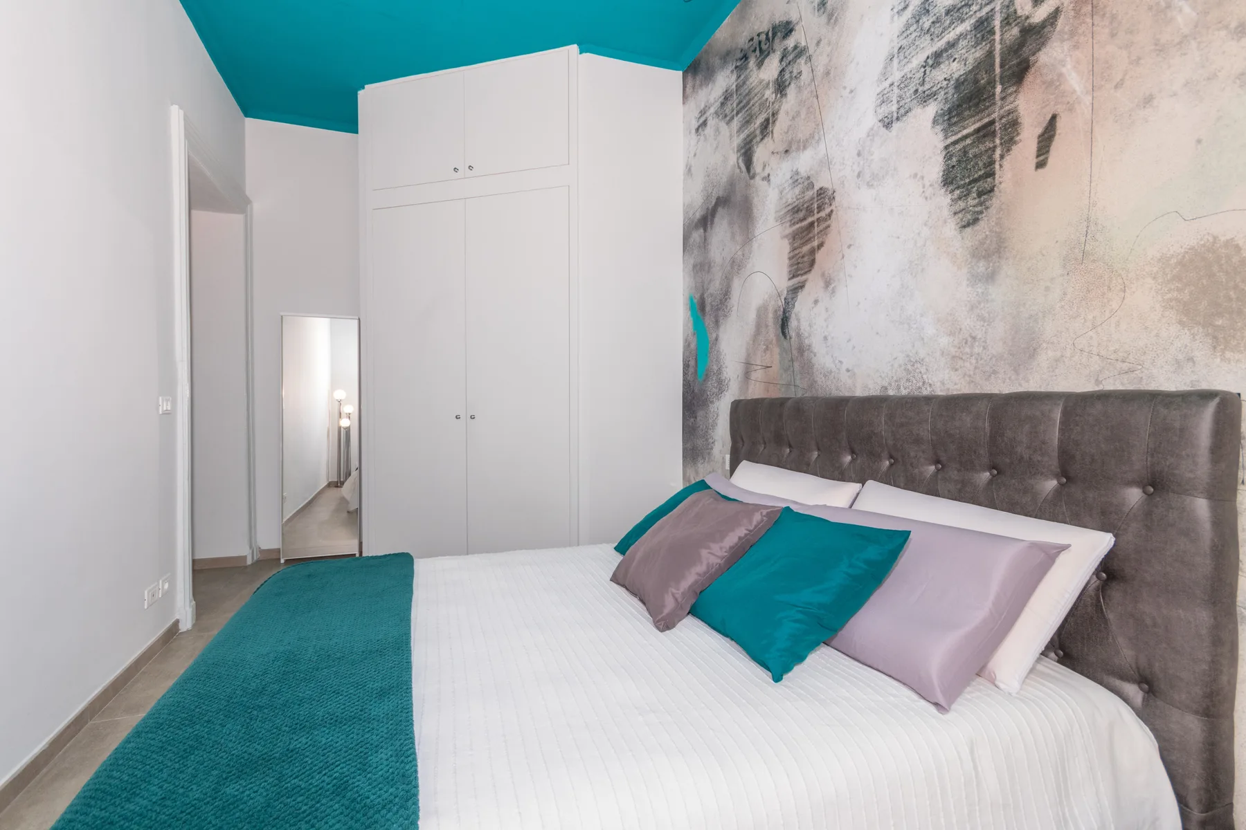 A bedroom with a bed dressed in white and teal bedding.