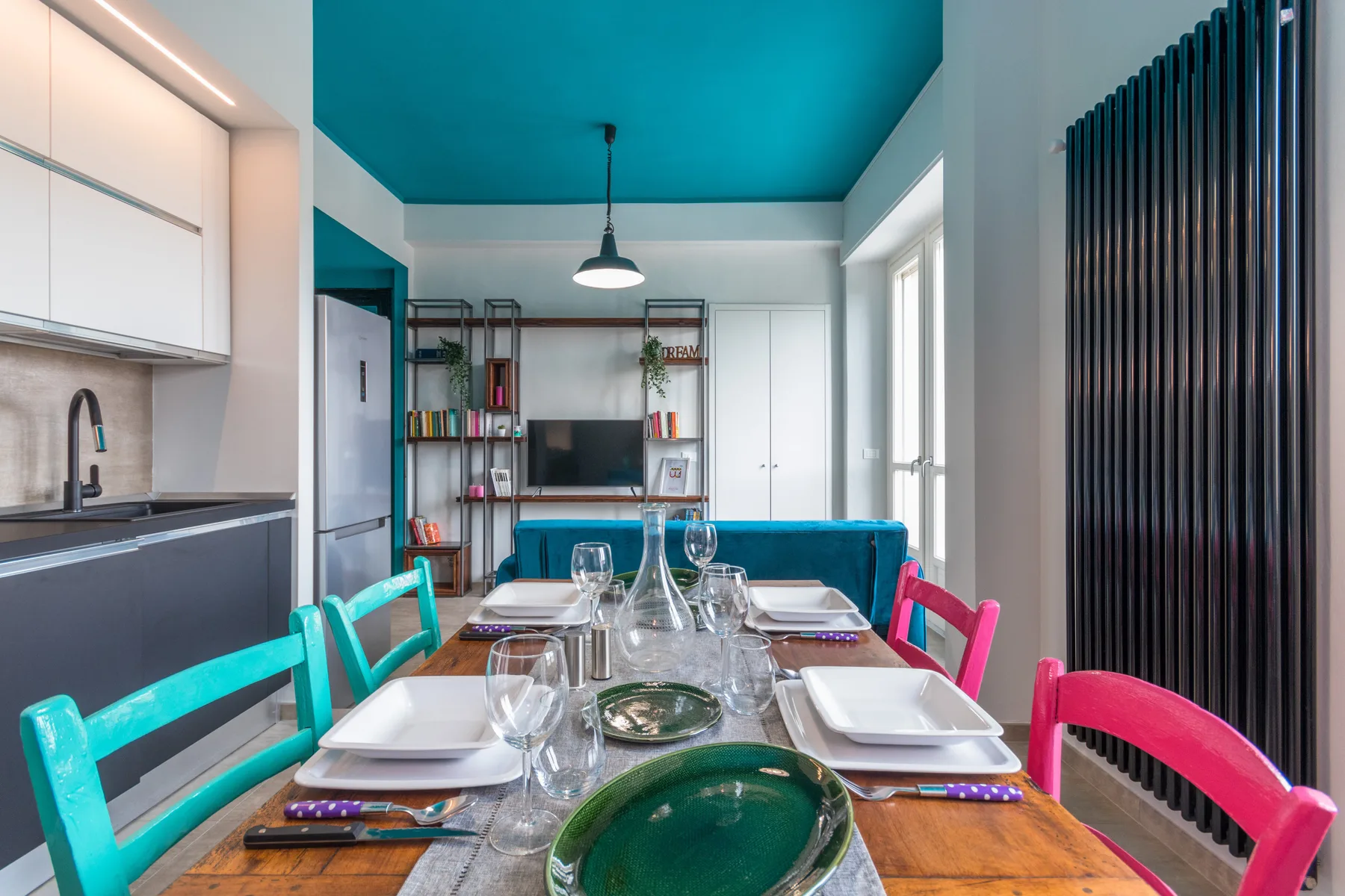 A dining table with colorful seating fills a bright open-plan kitchen and living area.