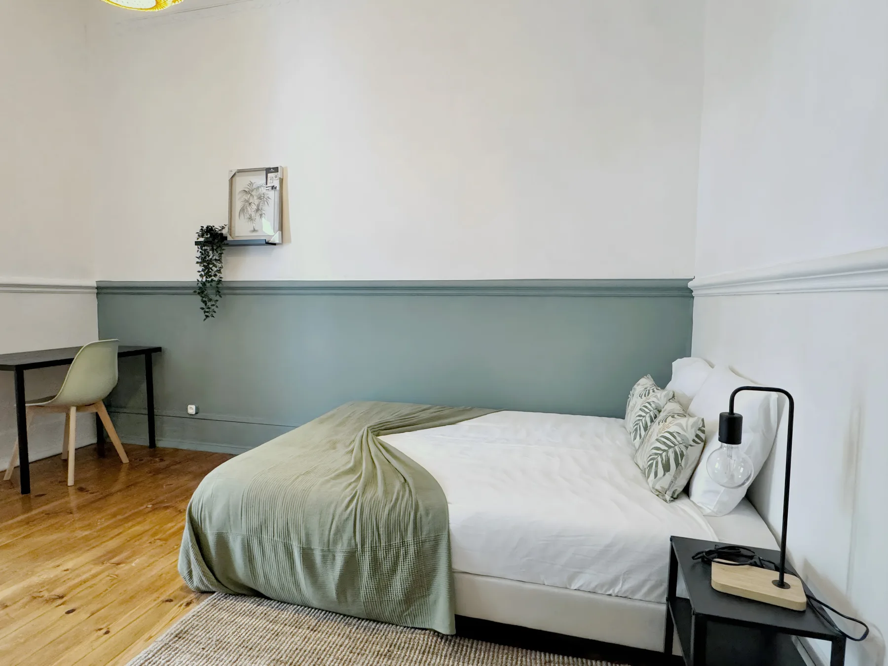 A bedroom with a bed, green bedding, and a small desk.