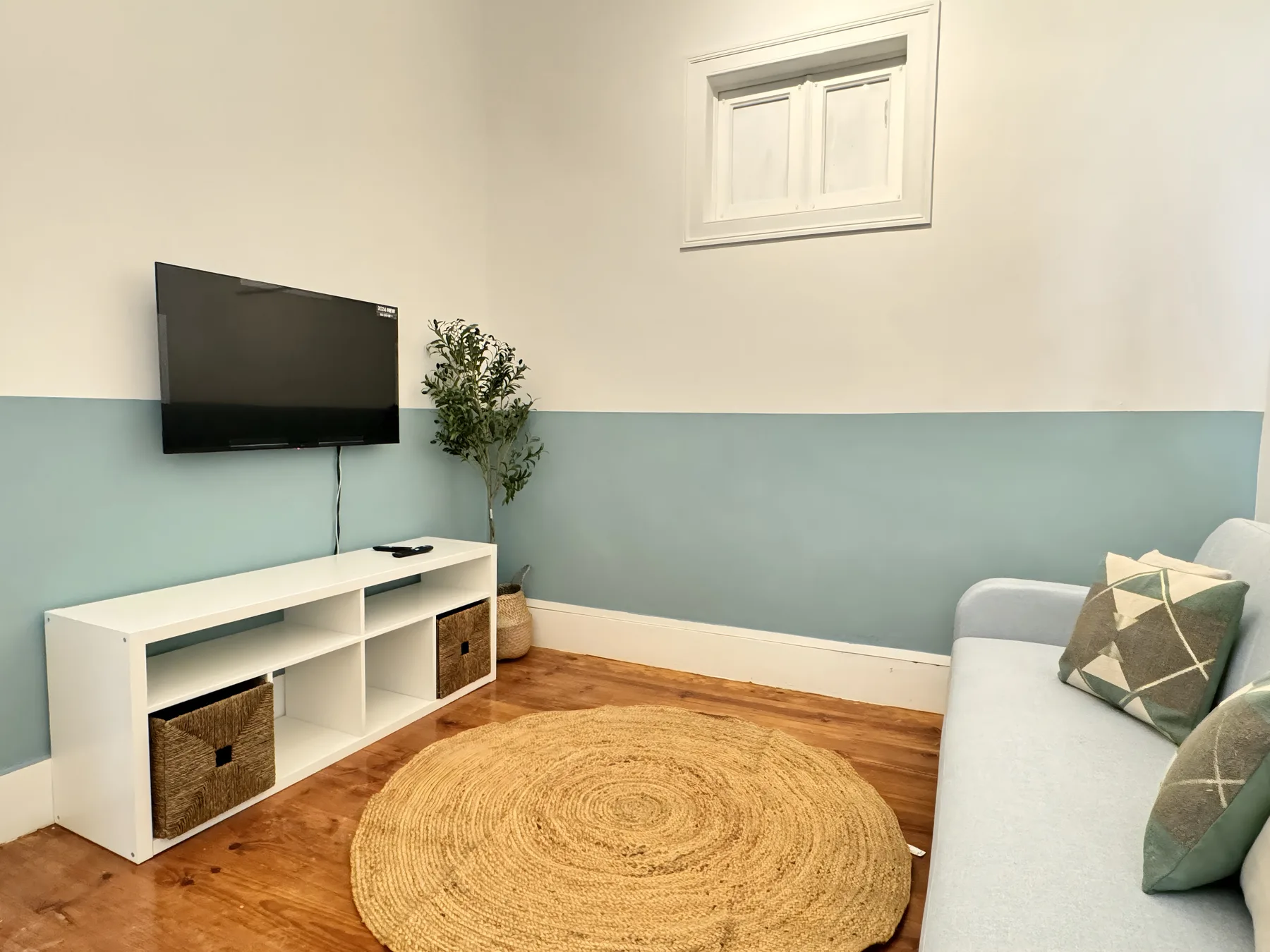 Living room with a television, light-colored seating, and a round woven rug.