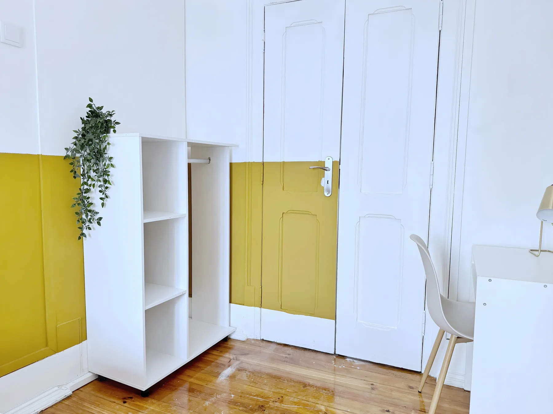 A bright room with a white desk, open shelving, and a yellow-painted wall.