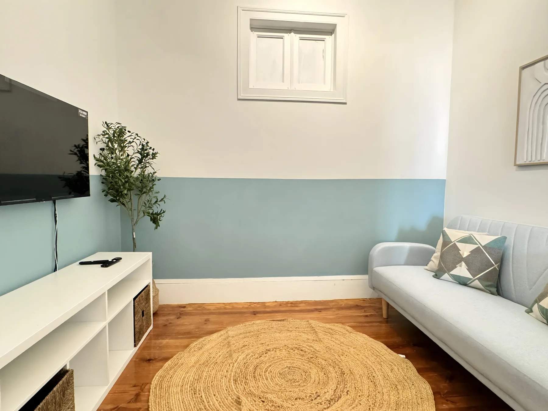 A living room with a light-colored sofa, wall-mounted television, and round woven rug.