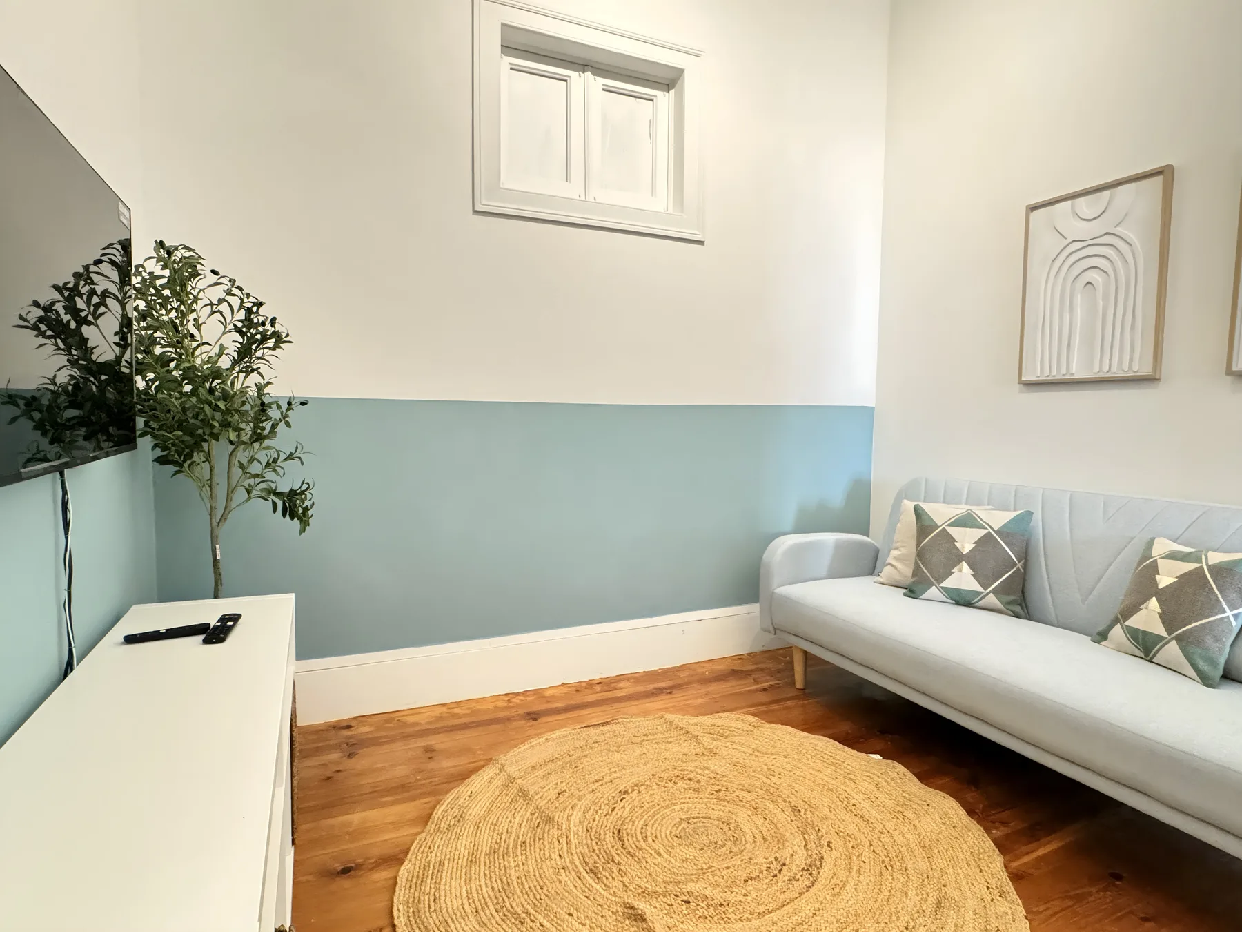 A living room with a white sofa, a television, and a round woven rug.
