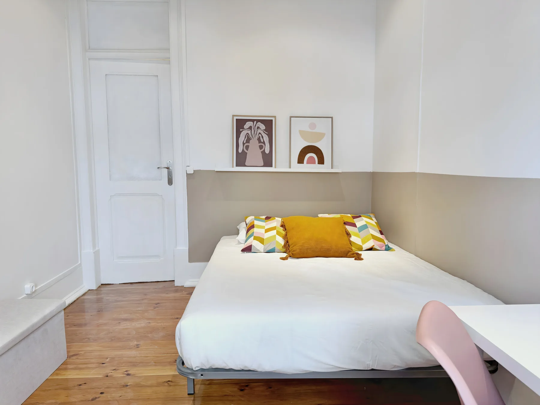 A bedroom with a white bed, colorful pillows, and framed prints.